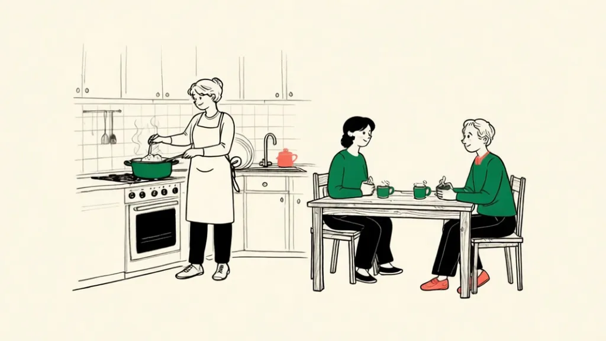 A volunteer in an apron stirring a pot in a shared guest-house kitchen while two guests sit at a table with mugs of tea