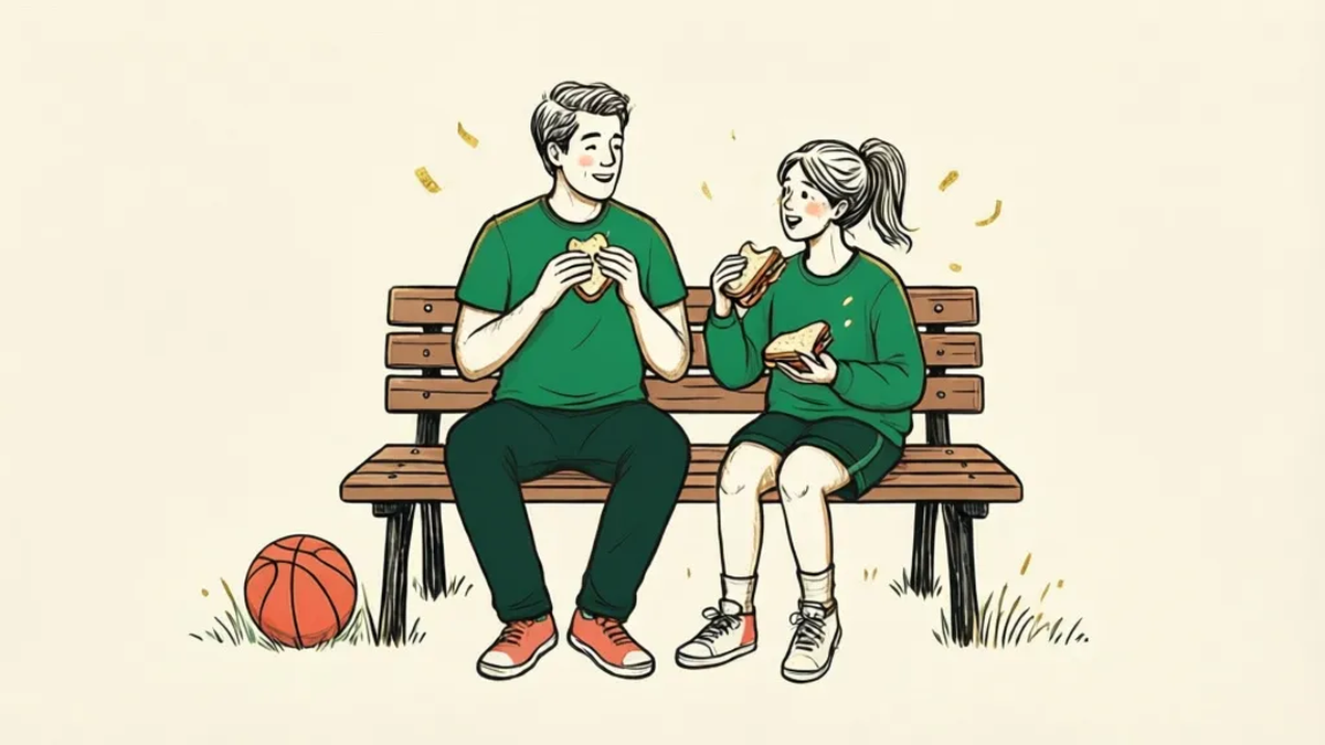 An adult and a young person sitting on a park bench sharing sandwiches and talking, a basketball on the grass beside them